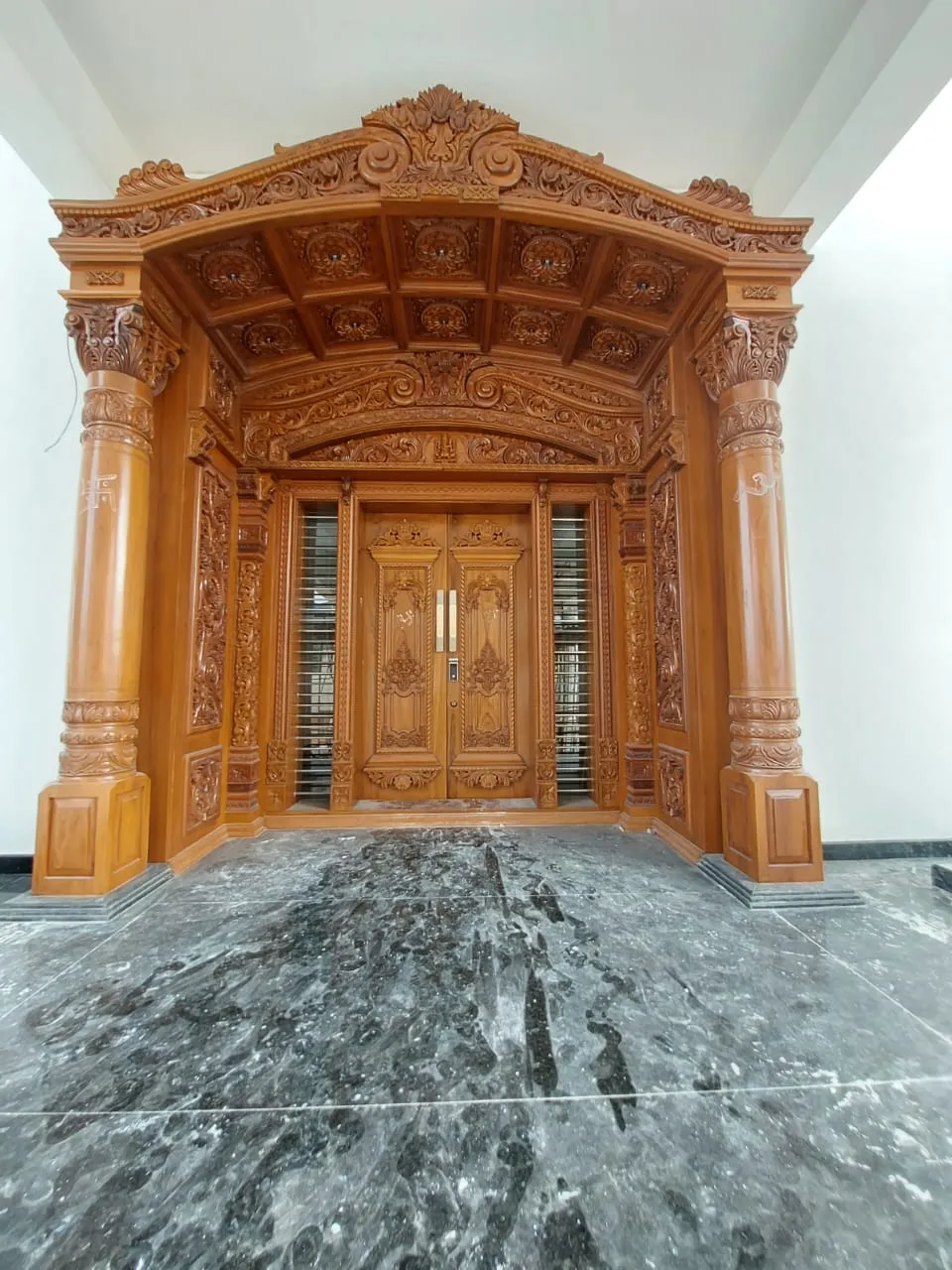 Carved teak entrance with a tall arched crown and brass detailing